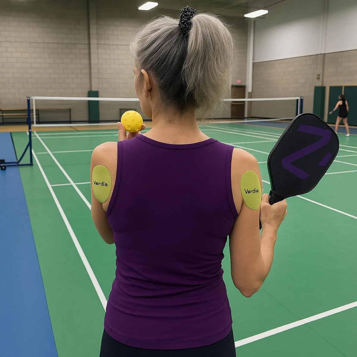 A woman on a pickleball court seen from behind, wearing patches on both shoulders.